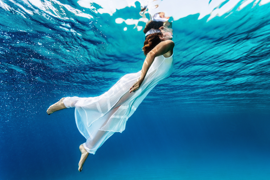 Nice girl emerges from the sea, swimming underwater, enjoying nice refreshing water, wearing long dr
